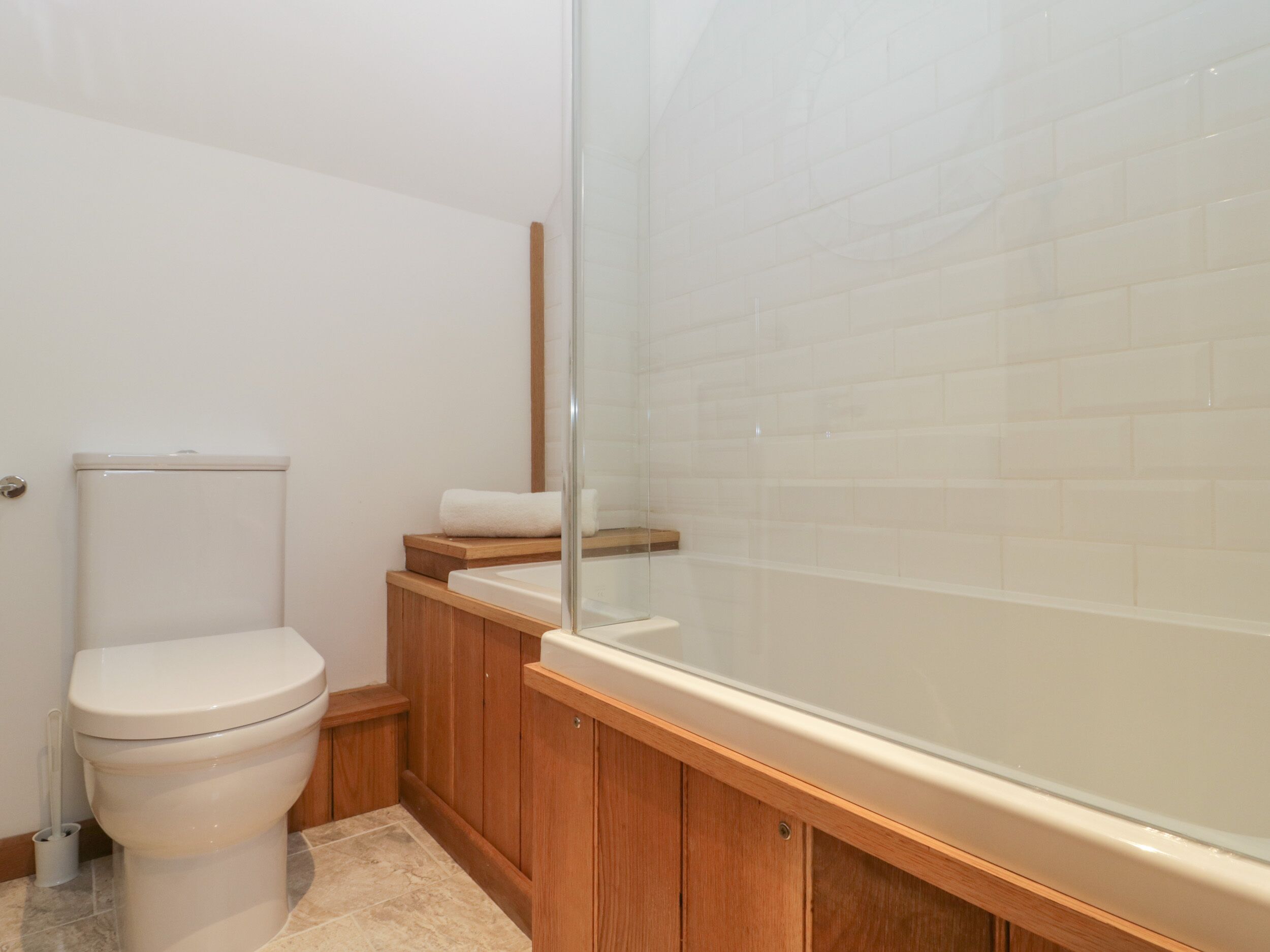 Un baño con inodoro, armarios de madera, cabina de ducha de vidrio y pared con azulejos.