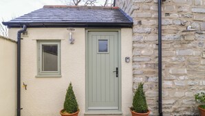 Une petite maison avec une porte verte, une fenêtre et deux plantes en pot.