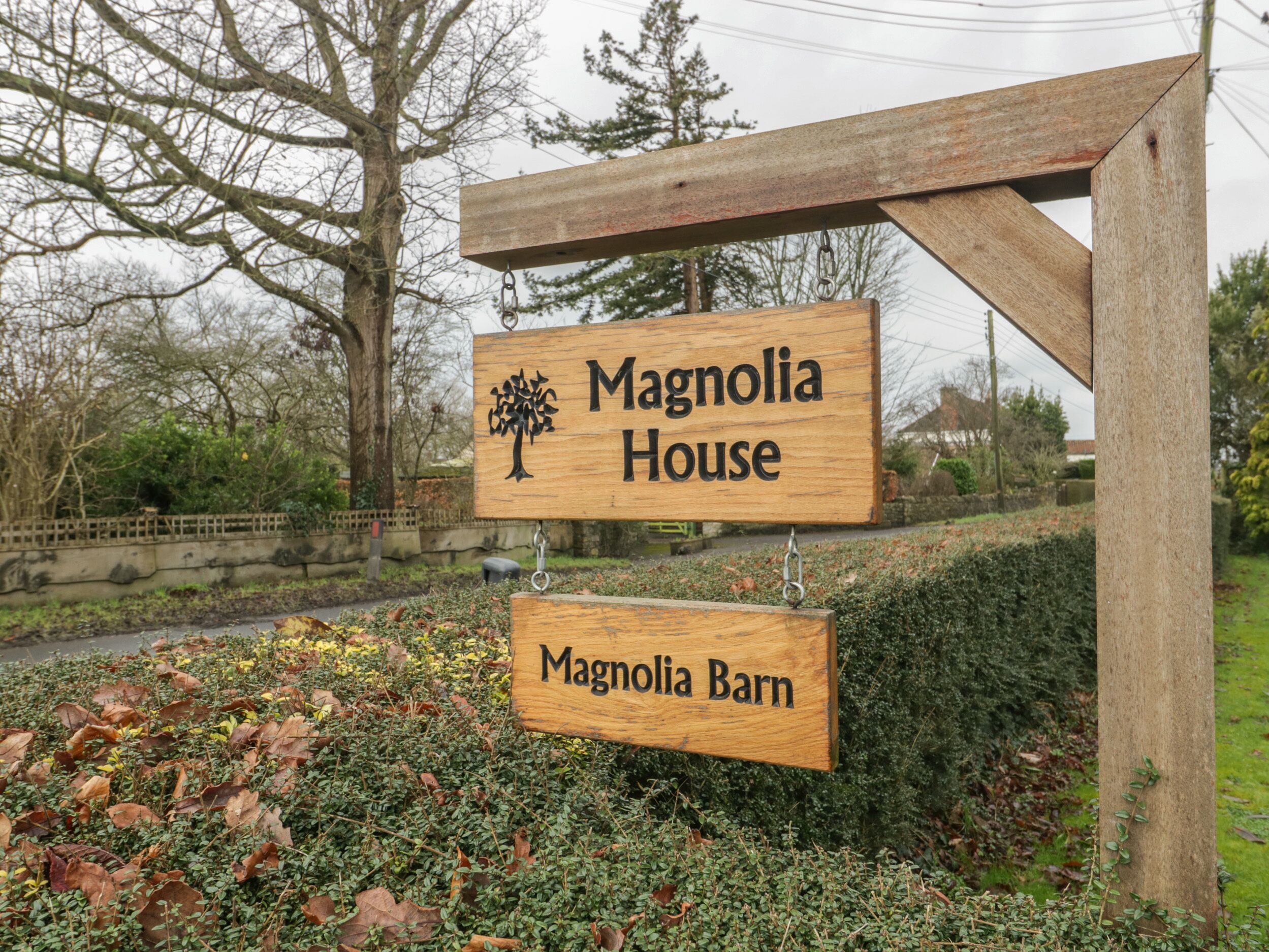 A wooden sign with 'Magnolia House' and 'Magnolia Barn' written on it, mounted on a post with a chain link.