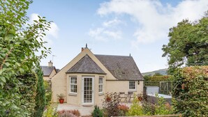 Una casa encantadora con techo a dos aguas, puerta principal y un pequeño patio con mobiliario exterior.