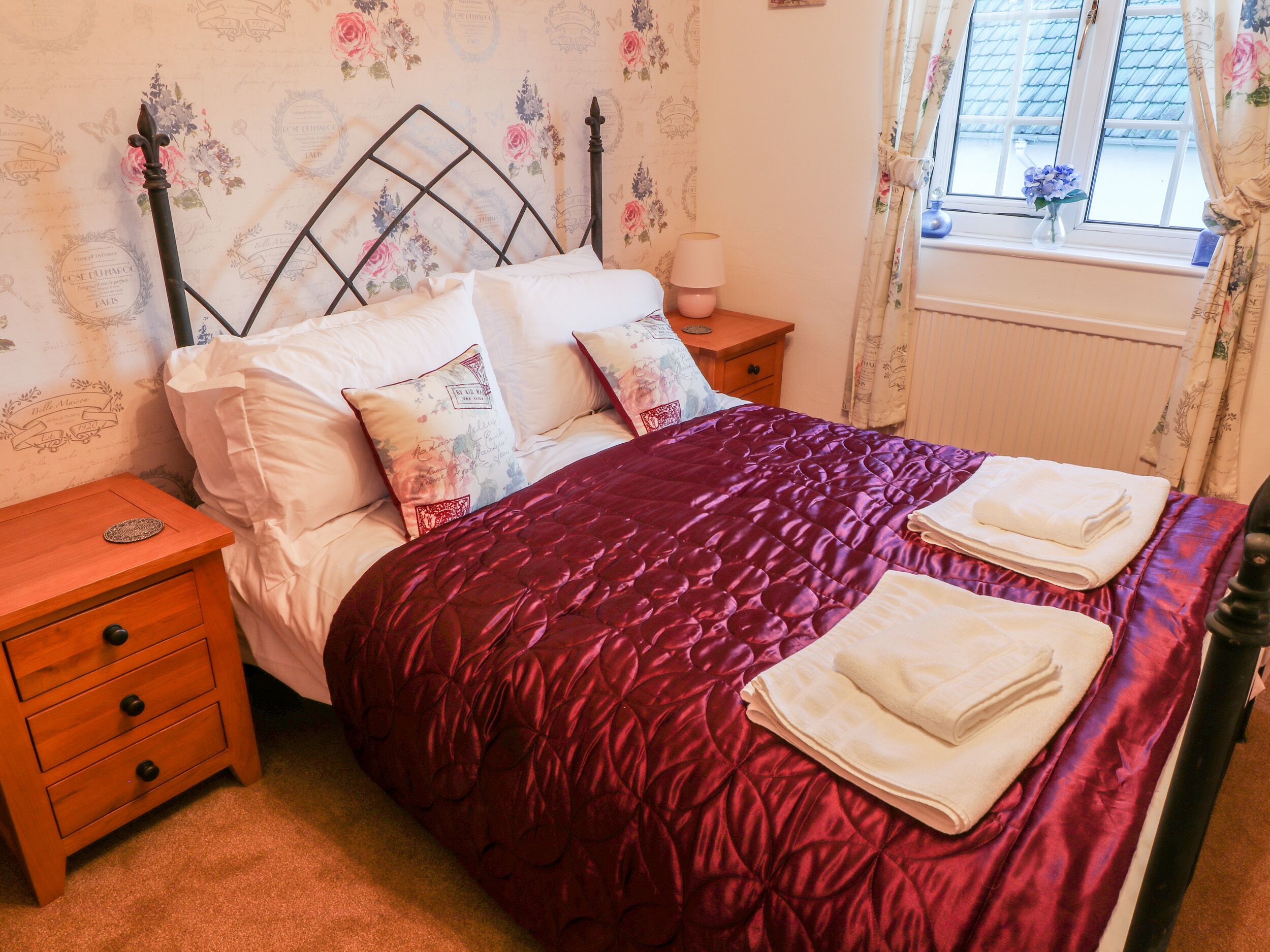 A neatly made bed with a red quilt, white pillows, and a wooden nightstand with drawers.