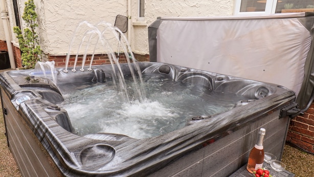 Ein Whirlpool mit mehreren Düsen, eine Flasche Roséwein und eine Schale Erdbeeren auf einem kleinen Tisch daneben.