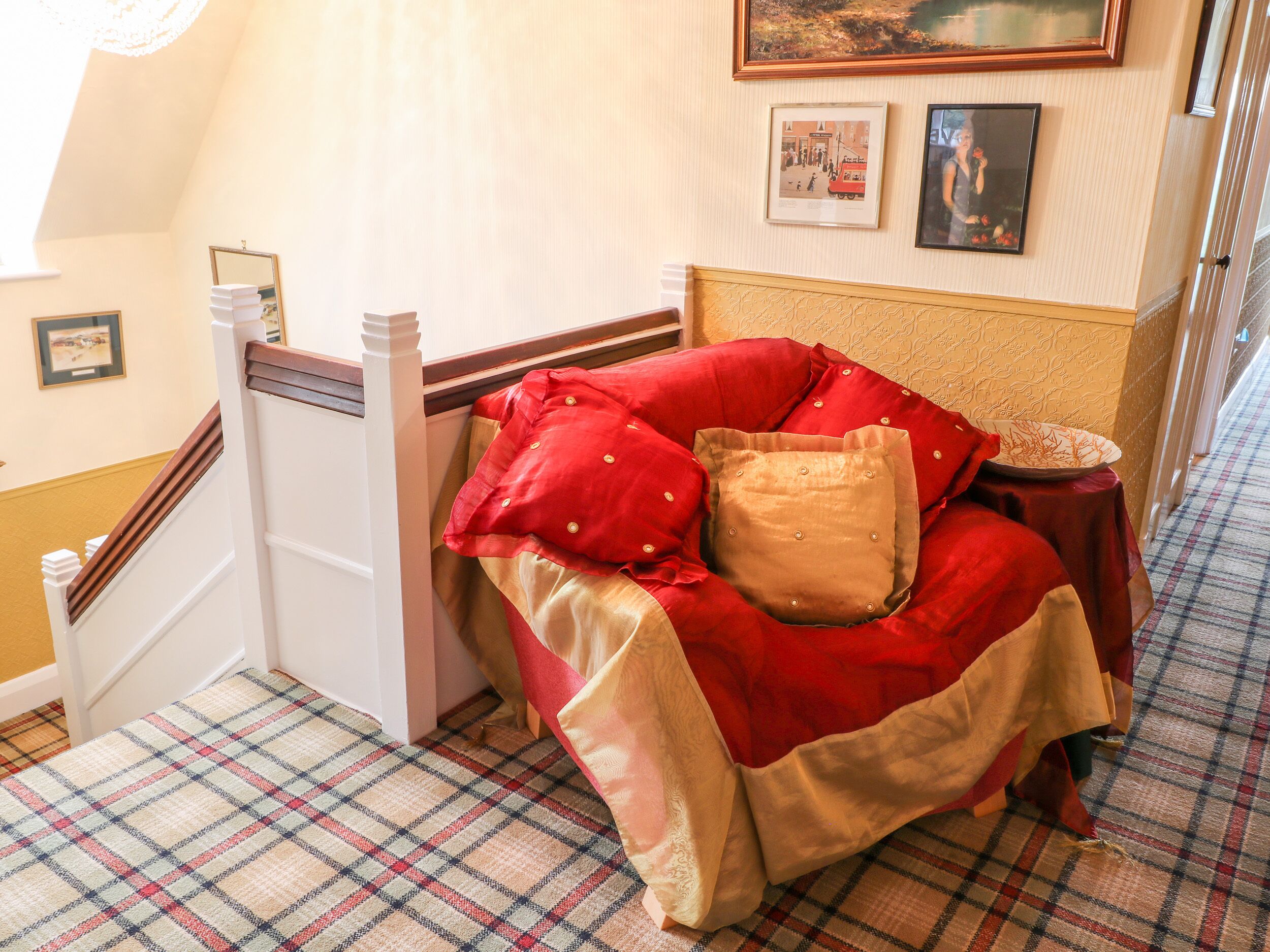 Un dormitorio con una cama cubierta con ropa de cama roja y dorada, un cabecero de madera y un suelo con estampado de cuadros.