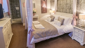 Ein Himmelbett mit Beige- und Weißtönen, ein Fernseher auf der linken Seite sowie ein Schminktisch mit Spiegel und Handtuchhalter.