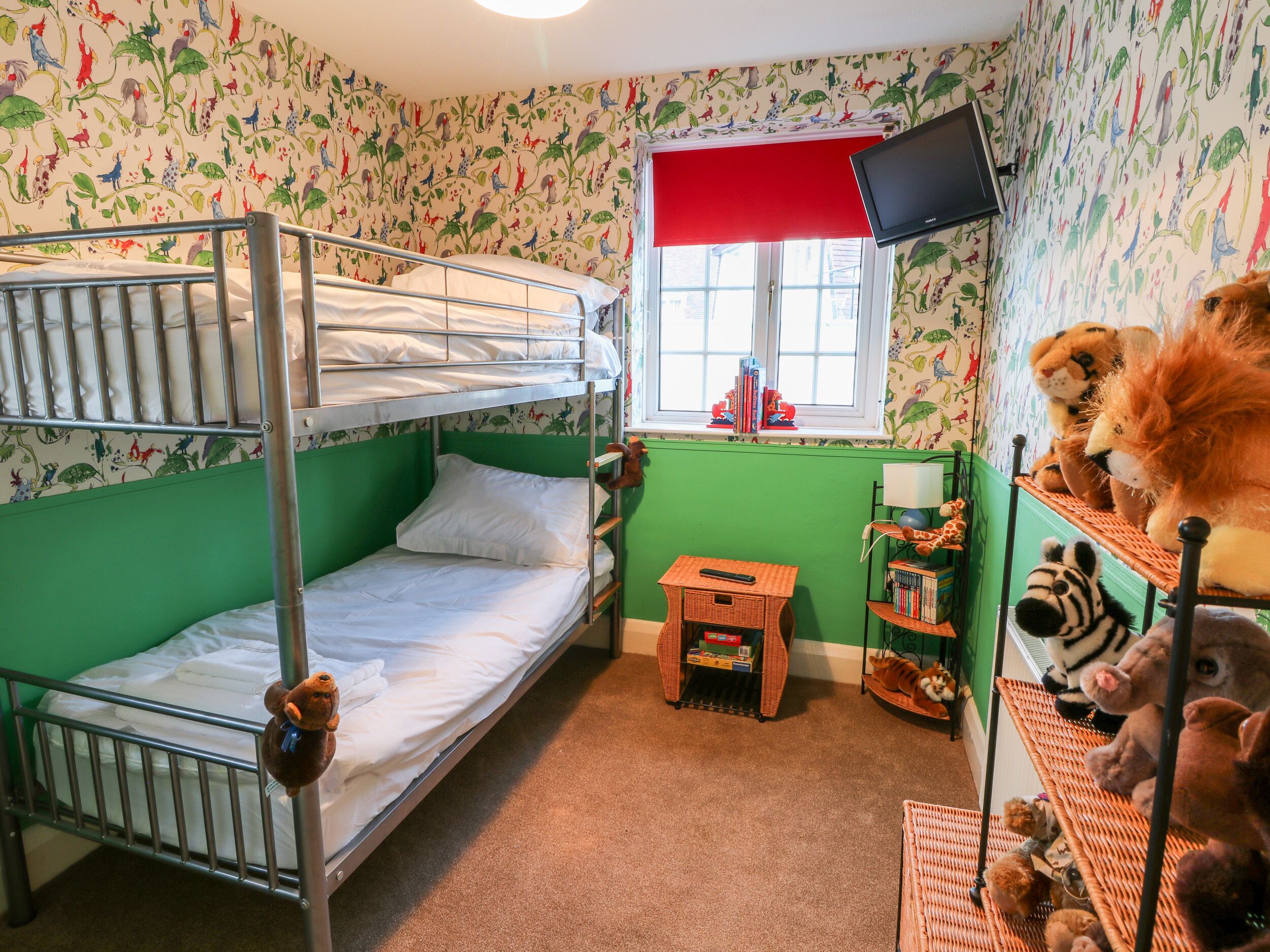 Une chambre avec un lit superposé, une fenêtre, un téléviseur et des étagères remplies de peluches.