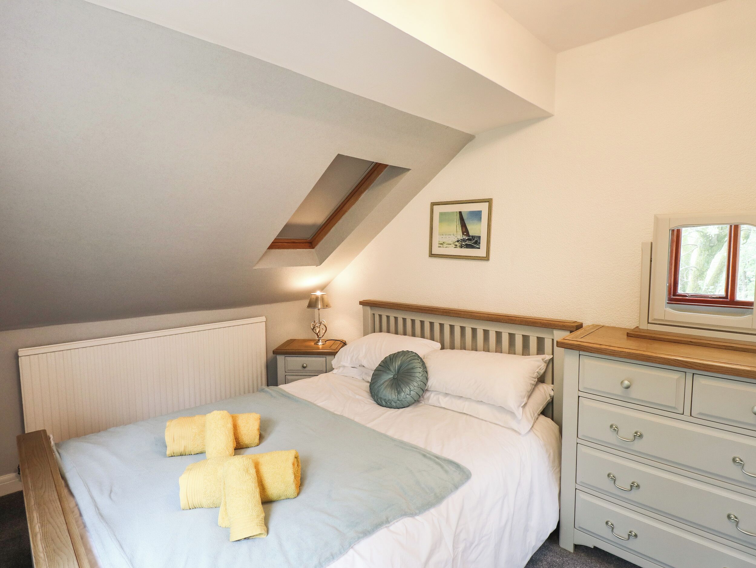 A bedroom with a bed, a nightstand, a dresser, a lamp, and a picture on the wall.