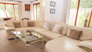 A living room with a beige sectional sofa, a glass coffee table, and a view of greenery outside.