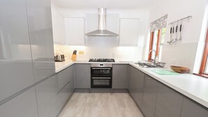 A modern kitchen with grey cabinets, a stainless steel range hood, a built-in oven, and a countertop with a sink and utensils.