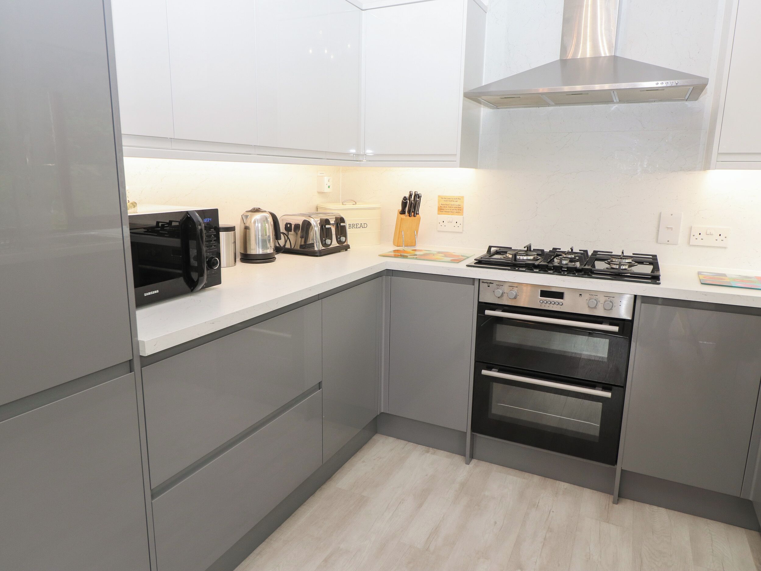 A modern kitchen with grey cabinets, a stainless steel range hood, a gas stove, a built-in oven, and a microwave.
