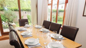 A dining table set for six with white plates, glasses, and cutlery, surrounded by dark leather chairs.