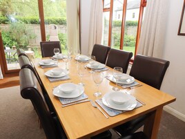 Mesa de comedor dispuesta para seis personas, con platos blancos, vasos y cubiertos, rodeada de sillas de cuero oscuro.