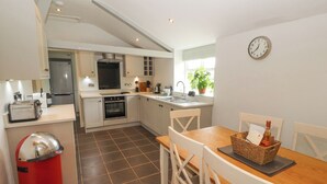A modern kitchen with a dining area, including a red trash bin, a wooden table, and white chairs. - Home Farm House (Penrith)