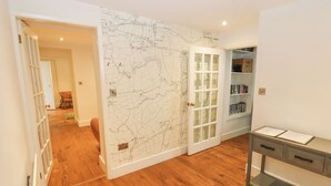 A room with a wooden floor, a map wall, a bookshelf, and a door leading to another room. - Home Farm House (Penrith)