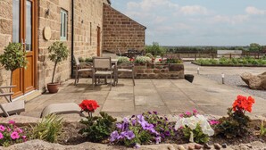 A stone building with a patio, outdoor seating, and flower beds. - Miller's Wheel (Harrogate)