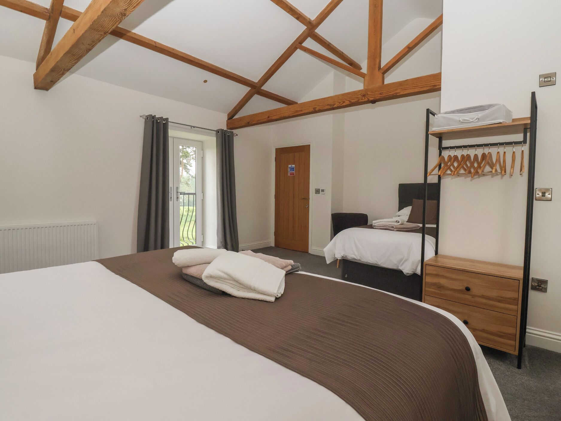 Une chambre d’hôtel avec un grand lit, un plus petit lit, une armoire, un radiateur, une porte et une fenêtre avec des rideaux.