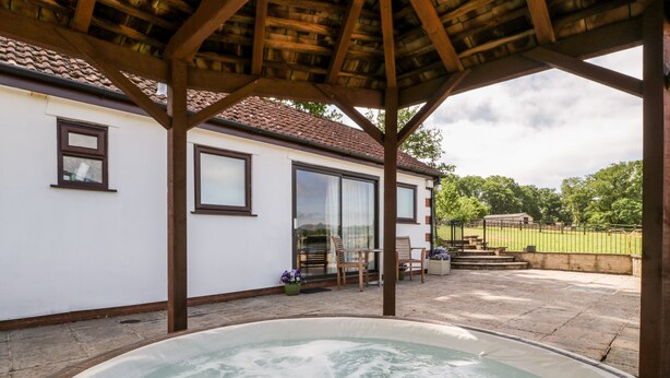 Un espace extérieur abrité comprenant un jacuzzi, une pergola en bois et une terrasse avec des chaises et une table.