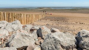 Une plage avec une clôture en bois et de gros rochers au premier plan.