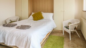 Une chambre à coucher avec un lit, un tapis vert, deux chaises en osier blanches et une armoire en bois.