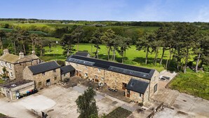 A stone building with a flat roof, a courtyard, and a view of a green field with trees. - Ploughman's Rigg (Harrogate)