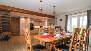 A dining area with wooden chairs and a table set for four, a kitchen in the background, and a staircase leading to another level. - Ploughman's Rigg (Harrogate)