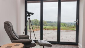 A modern room with a large sliding glass door leading to a patio, a reclining chair, a small round table, and a tripod with a camera. - Ploughman's Rigg (Harrogate)