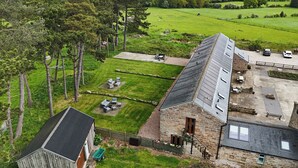 A stone building with a sloped roof, a fenced yard with outdoor seating, and a view of a green field. - Ploughman's Rigg (Harrogate)