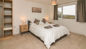 A bedroom with a large bed, a wooden wardrobe, a bedside table with a lamp, and a window with curtains. - The Outlook (Taunton)