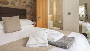 Habitación de hotel con pared de piedra, puerta de madera, baño con inodoro y lavamanos, y cama con ropa blanca y toallas.