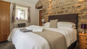 A bedroom with a stone wall, a bed with white linens, a wooden wardrobe, and a window with curtains. - Shepherd's Crook (Harrogate)