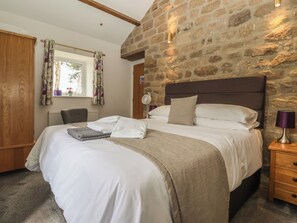 A bedroom with a stone wall, a bed with white linens, a wooden nightstand, and a window with curtains. - Shepherd's Crook (Harrogate)