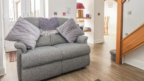 A grey sofa with a throw blanket and pillows, a wooden floor, a staircase, and a door with a window. - Shepherd's Crook (Harrogate)