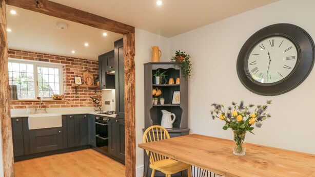 Een keuken met donkere kastjes, een houten bankje, een eettafel en een klok aan de muur.