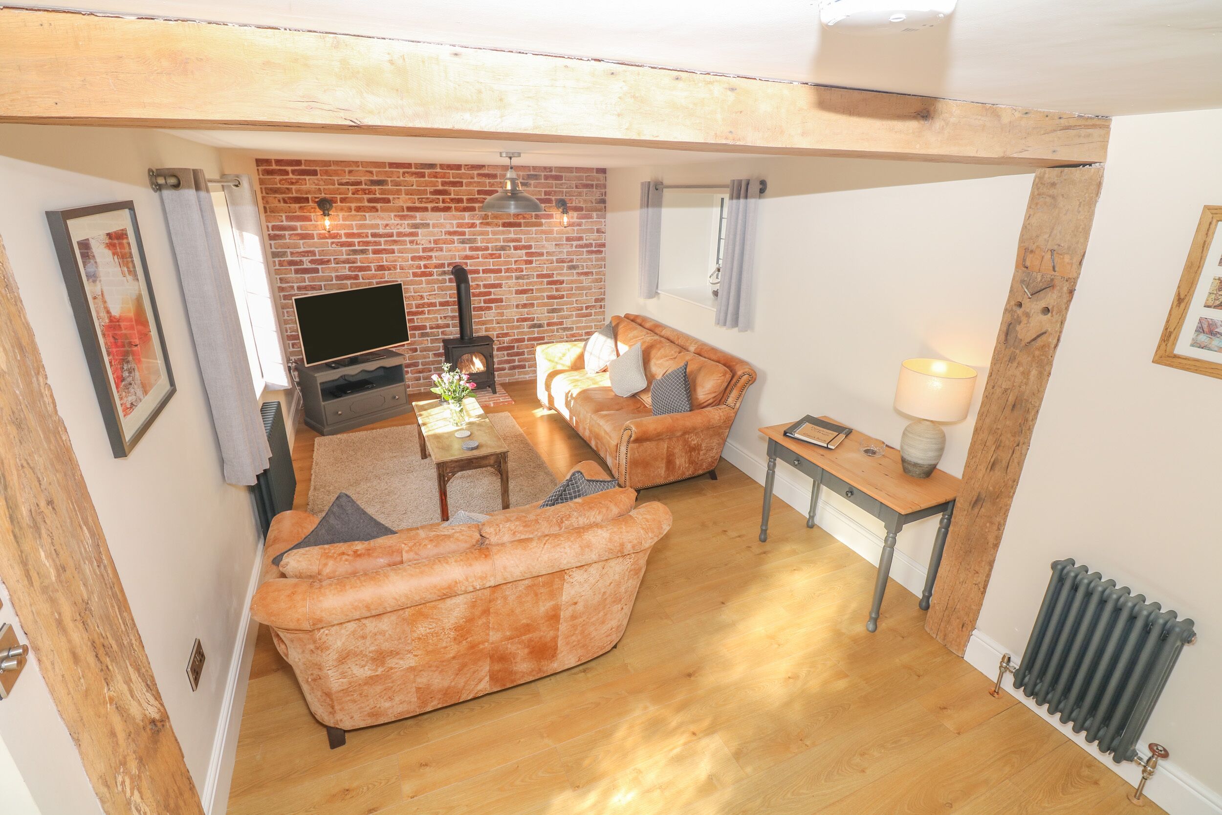 A cozy living room with a brick wall, wooden beams, a fireplace, and a television.