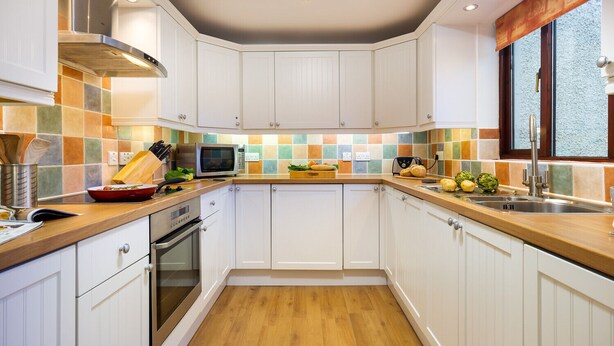 Una cocina moderna con armarios blancos, encimera de madera y salpicadero de azulejos.