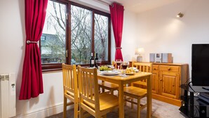 Un área de comedor con una mesa preparada para dos personas, sillas de madera, un televisor y un armario.