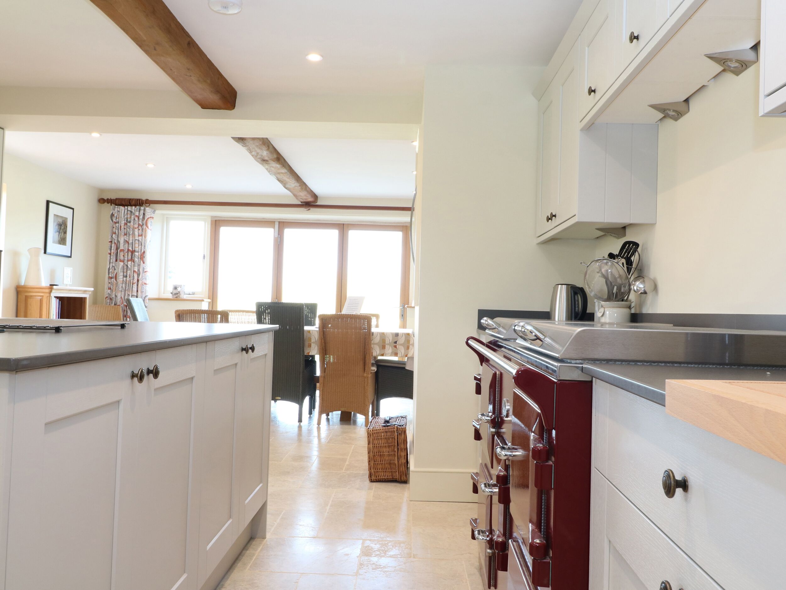 Una cocina moderna con armarios blancos, techo de vigas de madera y un comedor con mesa y sillas.