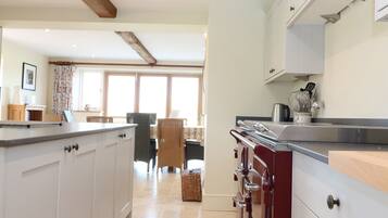Una cocina moderna con armarios blancos, techo de vigas de madera y un comedor con mesa y sillas.