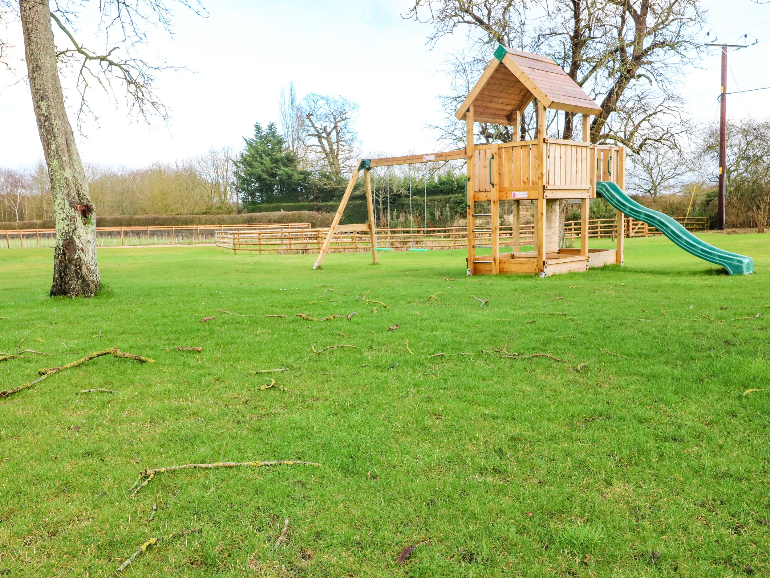 A wooden play structure with a slide and swings in a grassy park area.