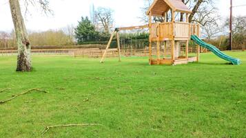 A wooden play structure with a slide and swings in a grassy park area.