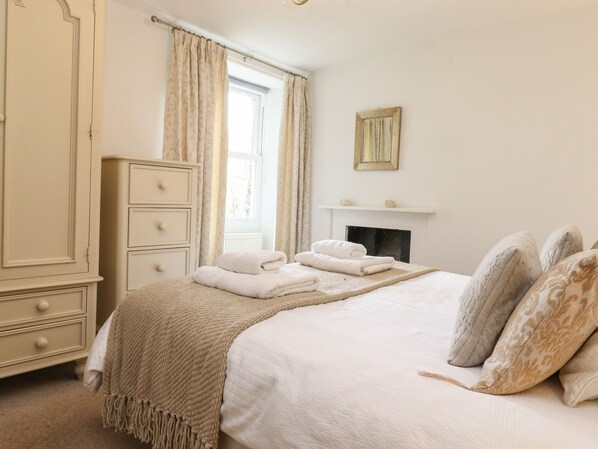 Un dormitorio con cama, cómoda, chimenea y ventana con cortinas.