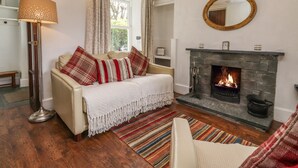 Una sala de estar acogedora con chimenea, un sofá con cojines escoceses, una lámpara de pie y una alfombra a rayas.