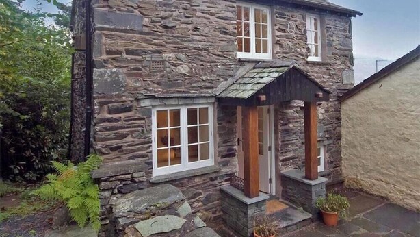 Una casa in pietra con due finestre e una porta di legno.