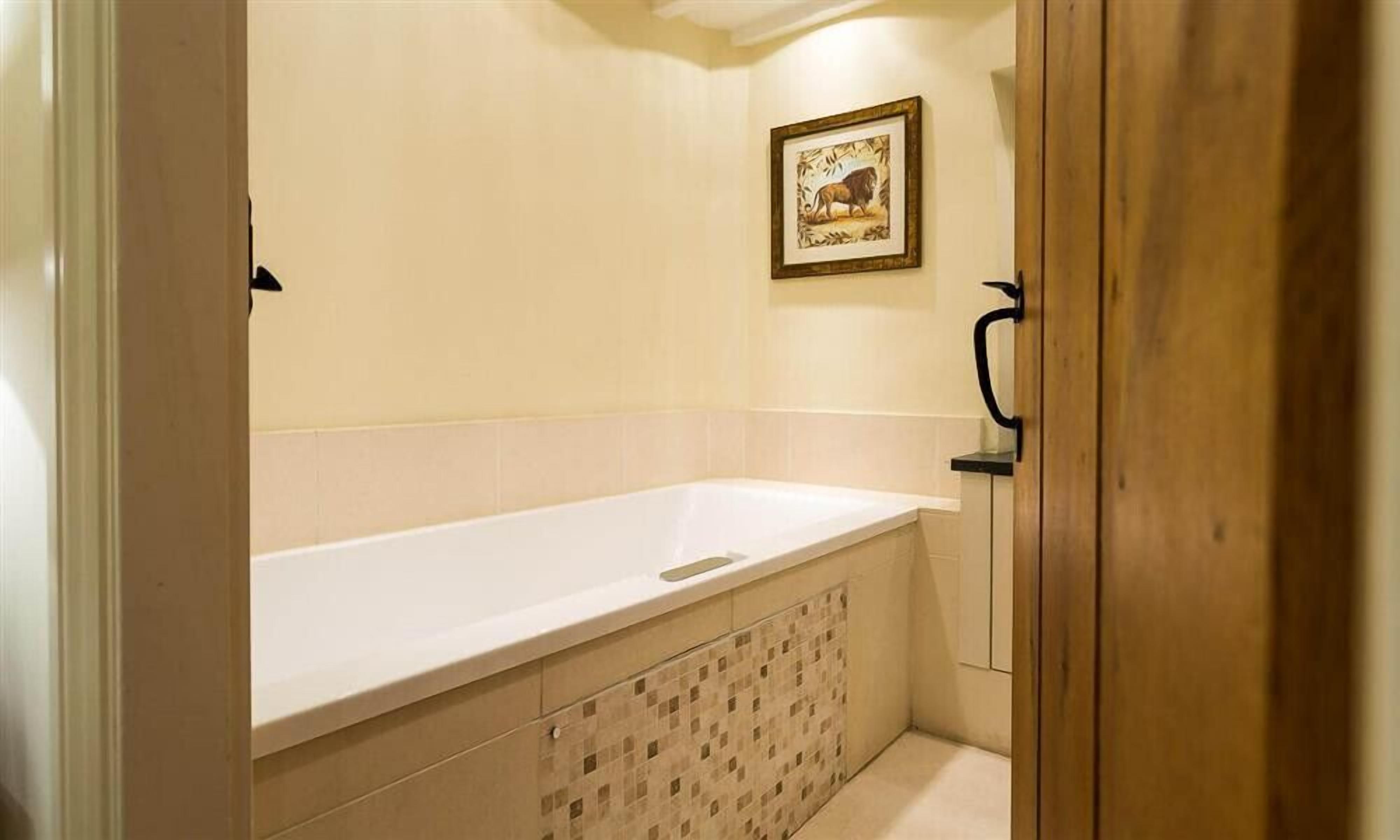 A bathroom with a white bathtub, a wooden door, and a framed picture on the wall.