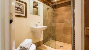 Un bagno con un lavandino bianco, cabina doccia in vetro e un quadro appeso al muro.