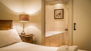 Camera d'albergo con un letto, una lampada da comodino, un bagno con lavandino e doccia, e un quadro appeso al muro.