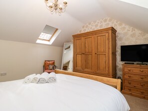 A bedroom with a large bed, a wooden wardrobe, a television, and a skylight.