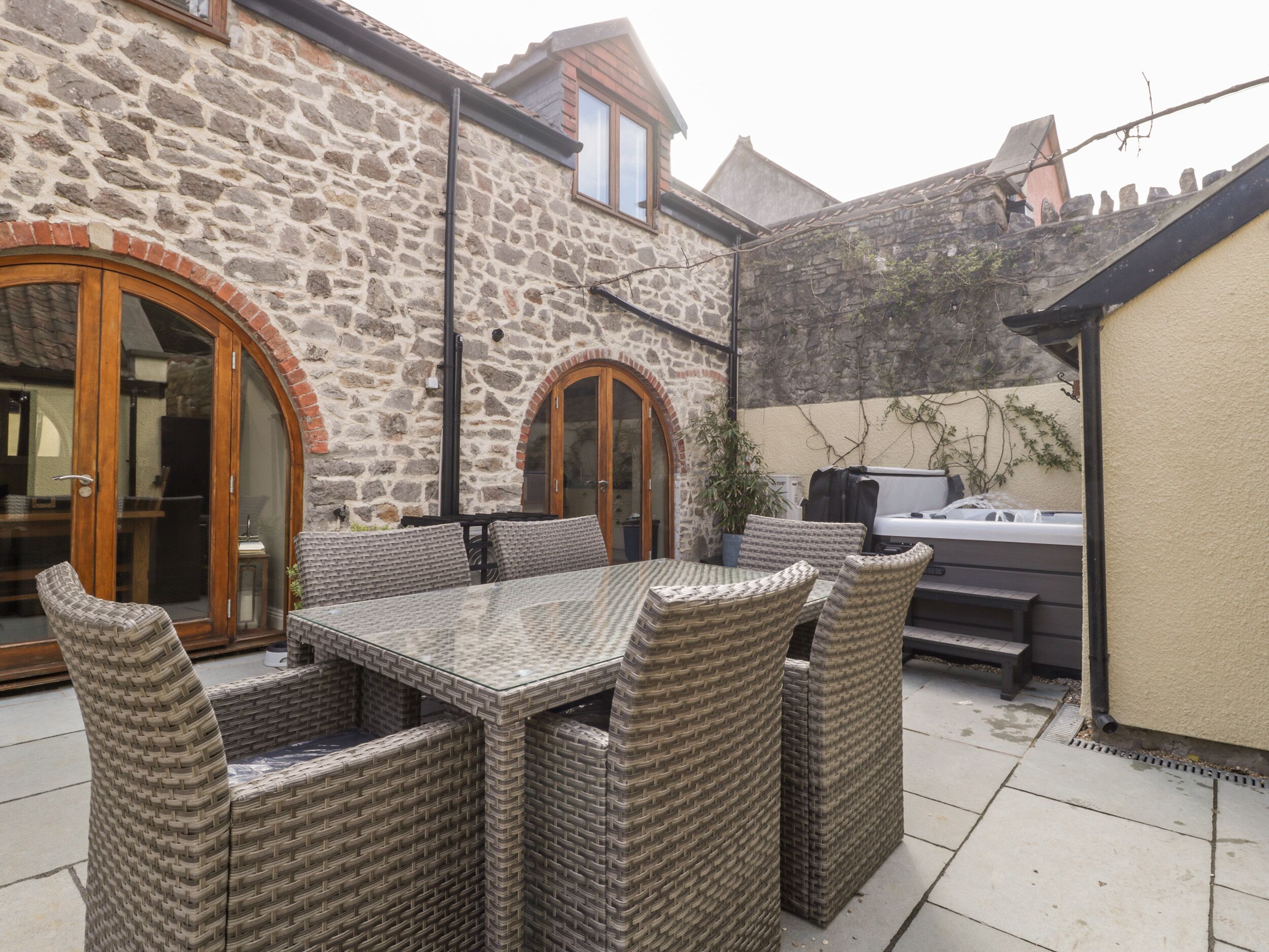 A stone building with a patio area featuring wicker furniture and a barbecue grill.