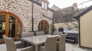 Ein Steinhaus mit einer Terrassenfläche, die Korbmöbel und einen Grill aufweist.