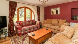 Ein Wohnzimmer mit einem roten Sofa, einem blumigen Sofa, einem Holztisch und einem großen Bogenfenster.