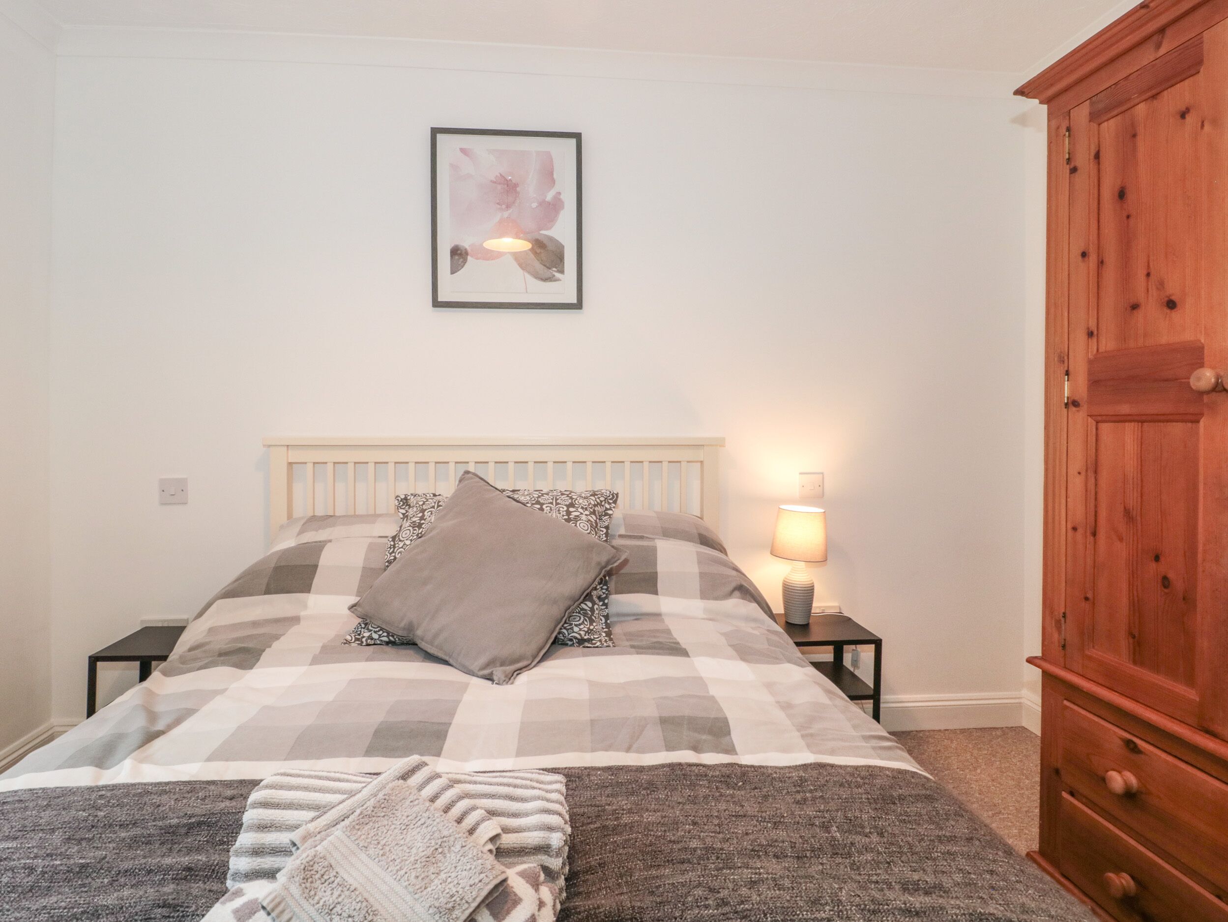 A bedroom with a bed, a bedside lamp, a wooden wardrobe, and a framed picture on the wall.
